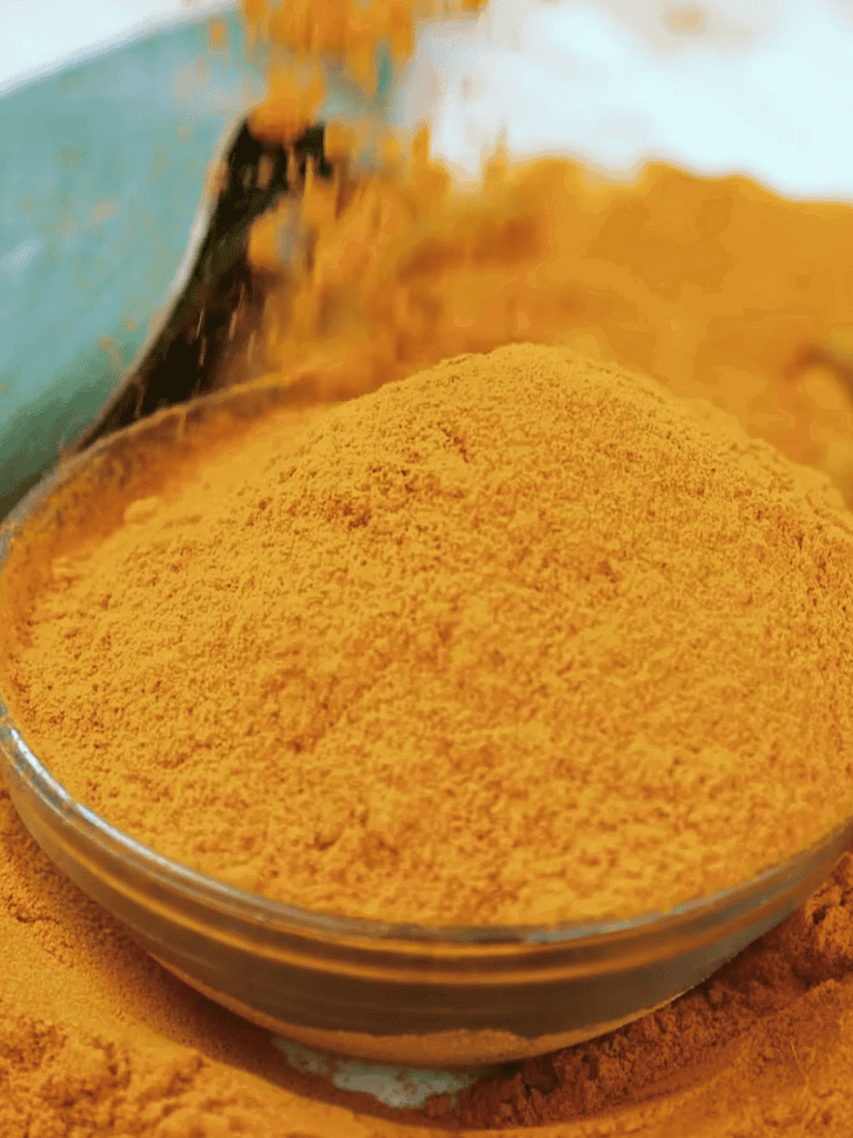 Close-up of vibrant yellow dog supplement powder in a glass bowl.