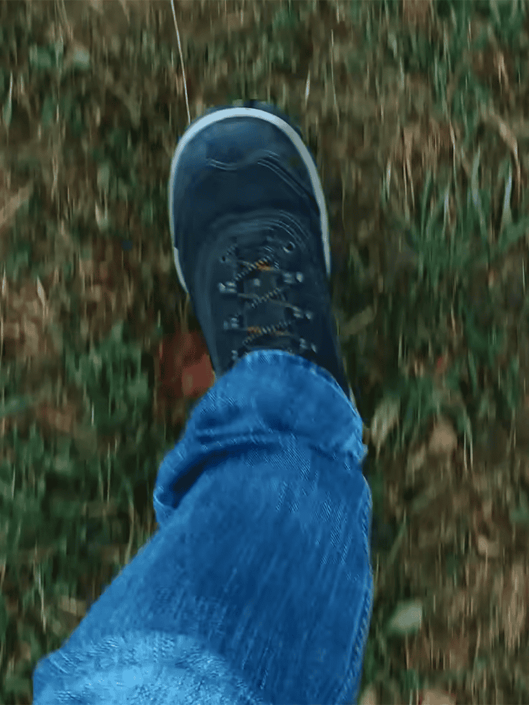 Close-up of a person's foot in a blue sneaker stepping on grass.