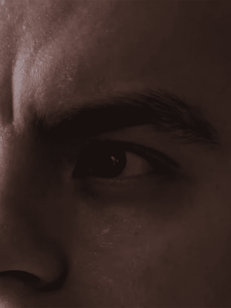 Close-up of human eye, detailed skin texture, dark tones, focused gaze.