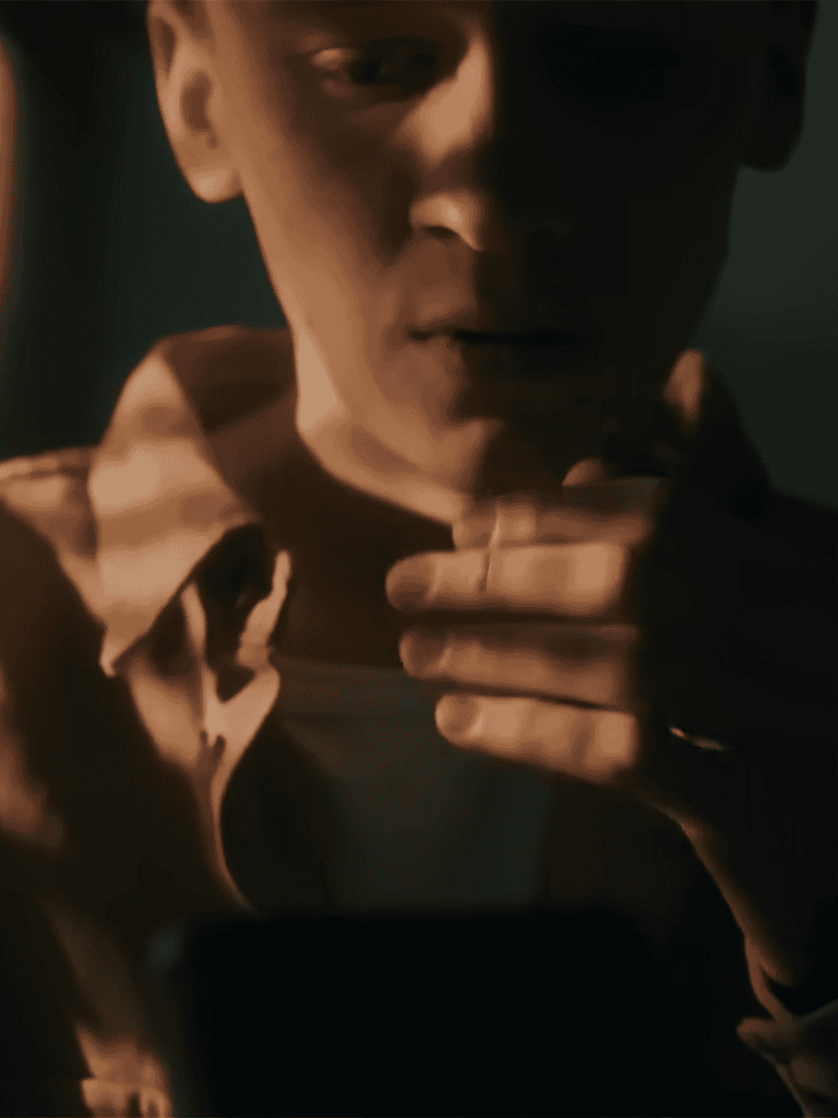 A close-up of a man with a serious expression, touching his chin thoughtfully in dim lighting.