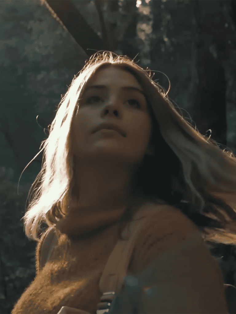 Woman in natural sunlight, forest background, casual attire, looking serene.