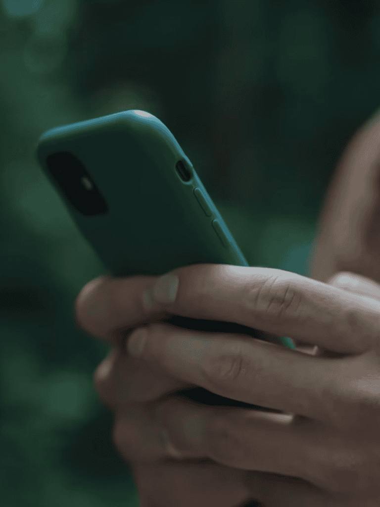 Close-up of a person holding a smartphone with blurred green background.