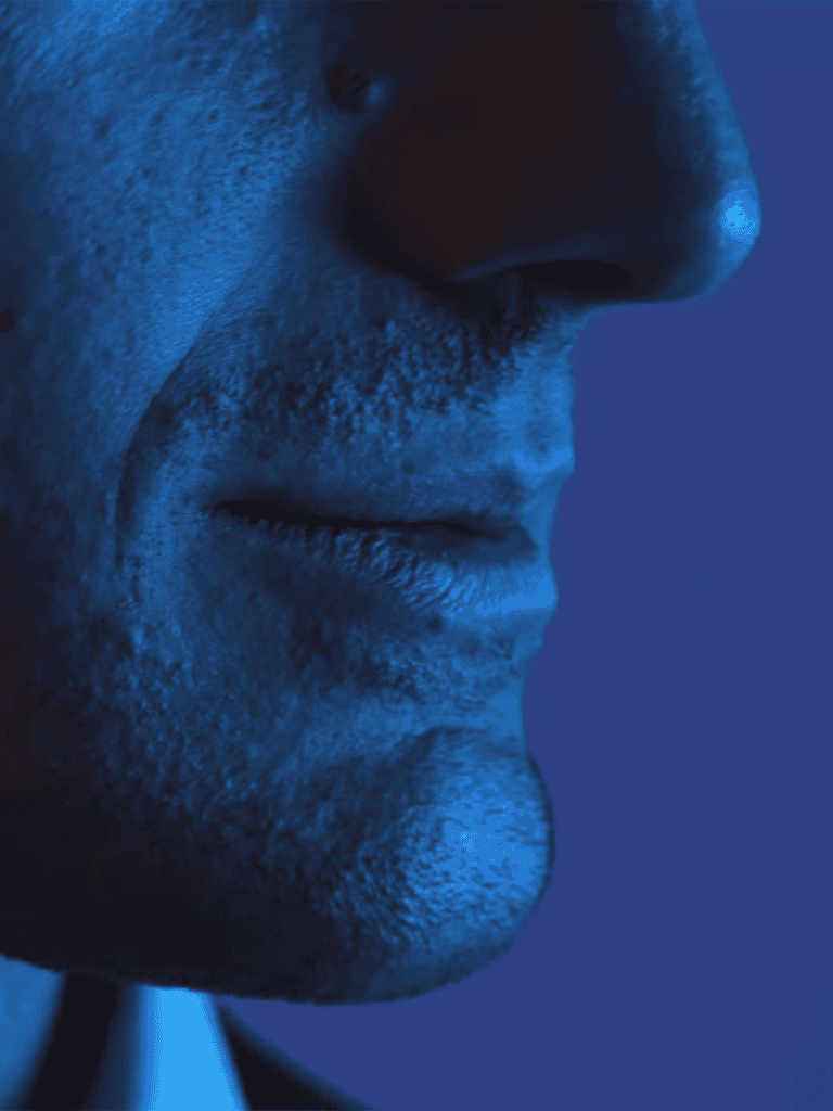 Narrow focus on man's lips and nose in blue lighting, highlighting skin texture and facial details.