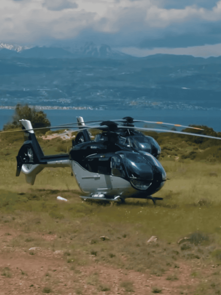 High-tech helicopter parked outdoors with scenic mountain and water background.