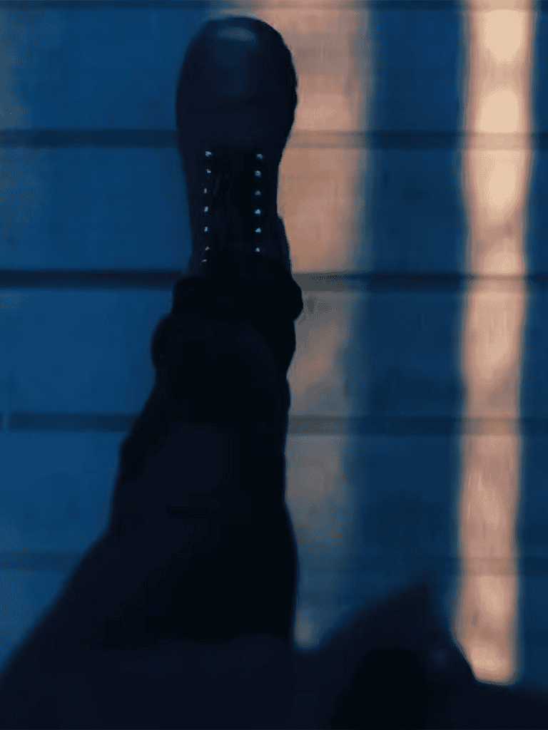 Close-up of a black boot on a wooden floor, with a reflection in the background.