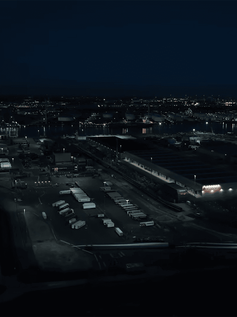 Night city port with trucks and warehouses illuminated during twilight, showcasing logistics and transportation infrastructure.
