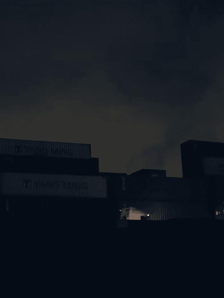 Dark warehouse with shipping containers at night, low lighting, industrial setting, no activity.