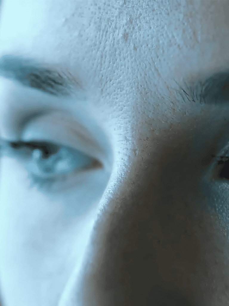 Close-up of a person's face with focus on skin texture and eyes, featuring a blue tint.