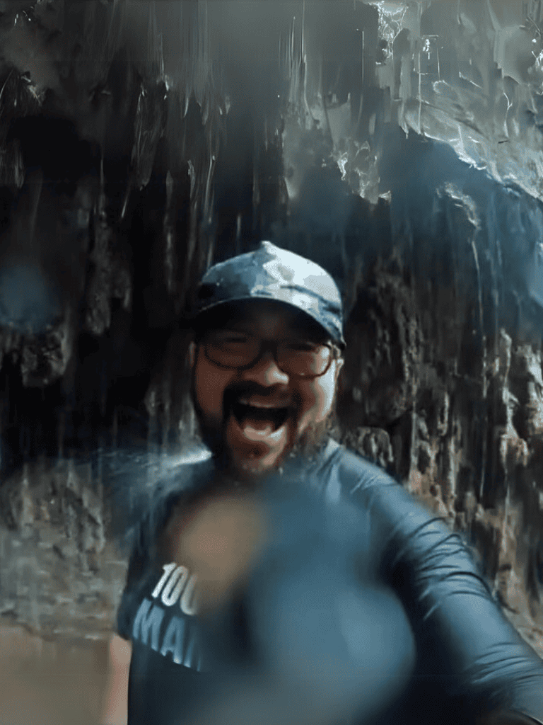 Hiker enjoying a refreshing moment under a waterfall during outdoor adventure.