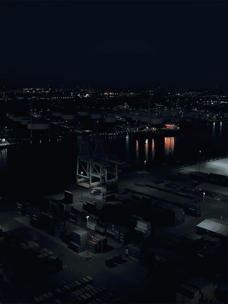 Nighttime dockyard with illuminated shipping containers and cargo cranes by water.