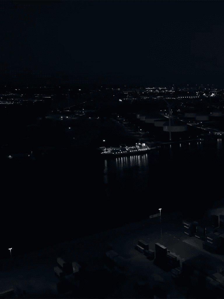 Night harbor with city lights and ships docked along the water.