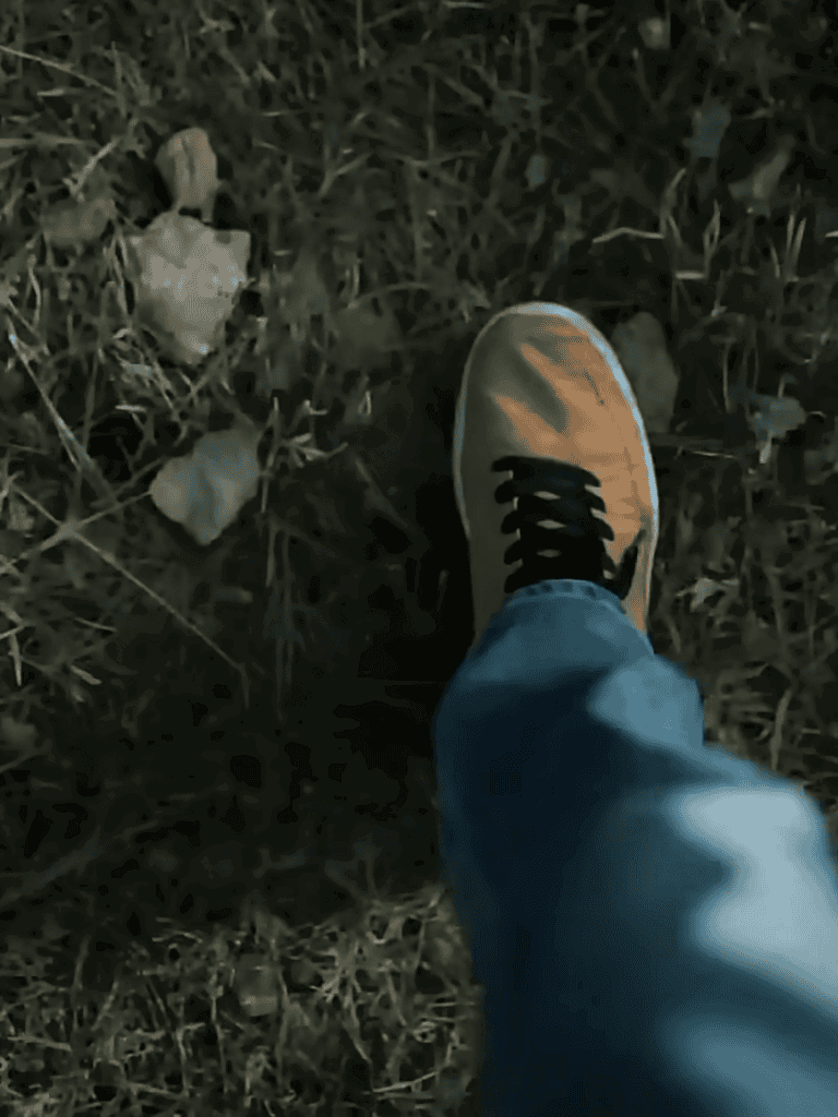 Close-up of a person’s foot wearing a yellow sneaker on dry grass outdoors.