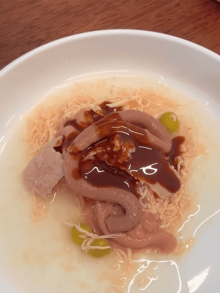 A bowl of shredded chicken in broth with gravy and green peas.