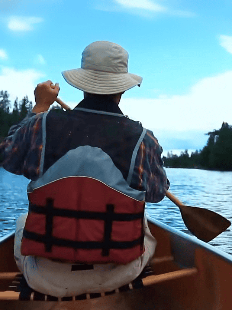 Fisherman paddling on calm river with lush greenery, enjoying outdoor water activity.